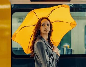 Person in a gray suit holding a yellow umbrella in a subway station