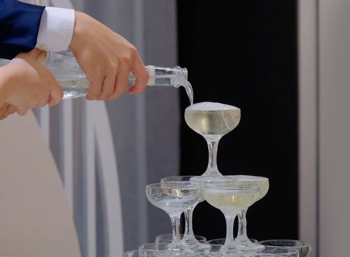 Pouring champagne over a tower of stacked glasses, depicting a celebratory or luxury setting