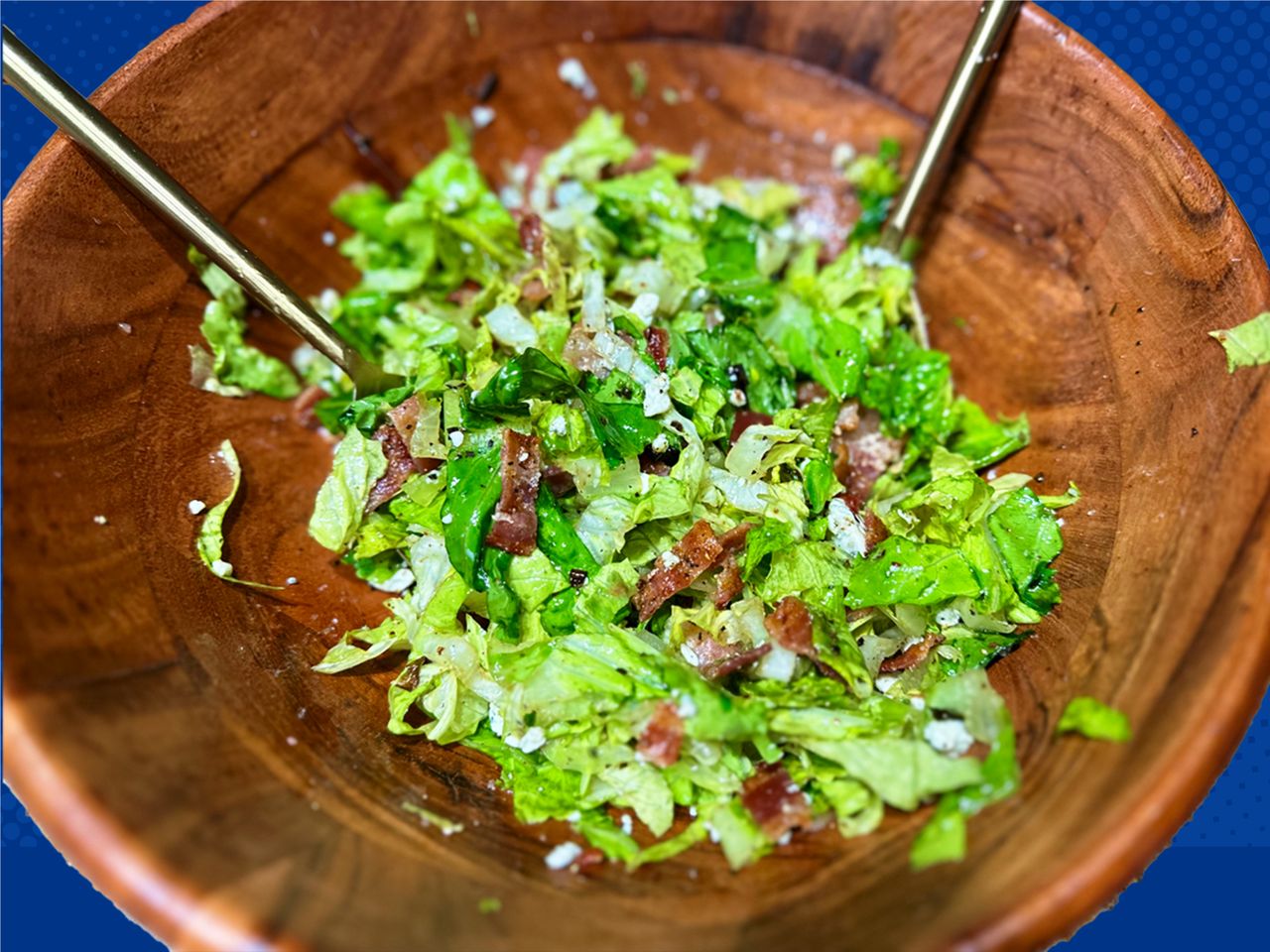 A wooden bowl of lettuce dotted with pieces of cooked bacon on a blue background.