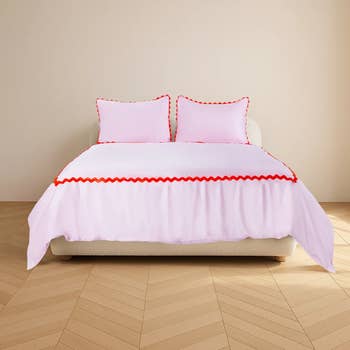 Bed with ruffled white bedding and red trim, two matching pillows; styled for a shopping catalog