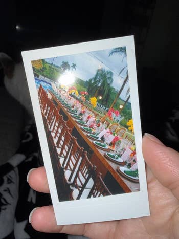 Polaroid photo of an elegant outdoor dining table set for an event, decorated with floral arrangements and wooden chairs