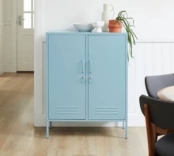 Light blue metal storage cabinet with drawers, adorned with potted plants and ceramic dishes, placed in a modern dining room setting
