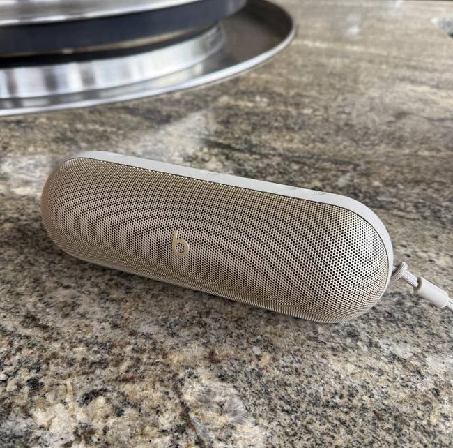 Portable wireless speaker in a sleek cylindrical design, resting on a stone surface
