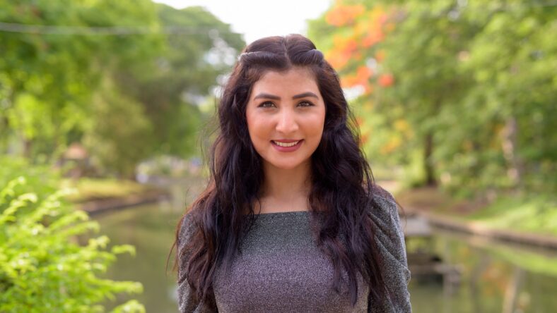 Portrait of young beautiful Indian woman relaxing at the park outdoors