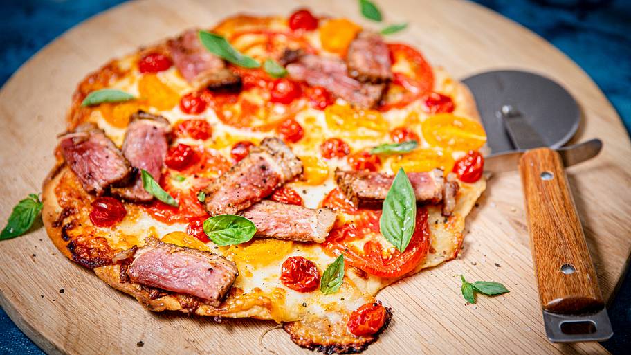 Freshly Prepared Pizza with Tomatoes, Steak, Basil, and Cheese on Wooden Plate
