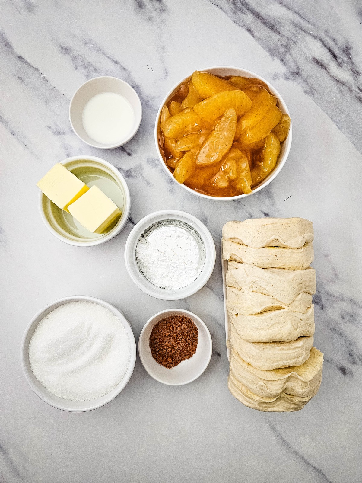 Ingredients for apple cinnamon biscuit loaf: canned biscuits, butter, sugar, cinnamon, apple pie filling, powdered sugar and milk