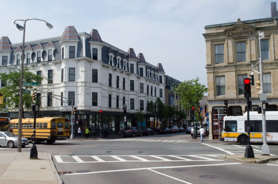 Street view of Nubian Square (formerly Dudley Square) in Roxbury, featuring historic buildings, traffic, and public transit in Boston.