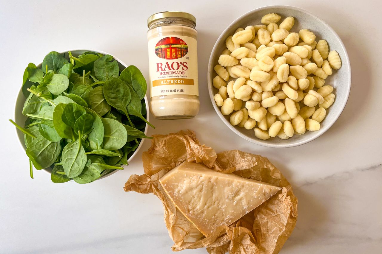 Ingredients for creamed spinach gnocchi including fresh spinach potato gnocchi a jar of Raos Alfredo sauce and a wedge of Parmesan cheese