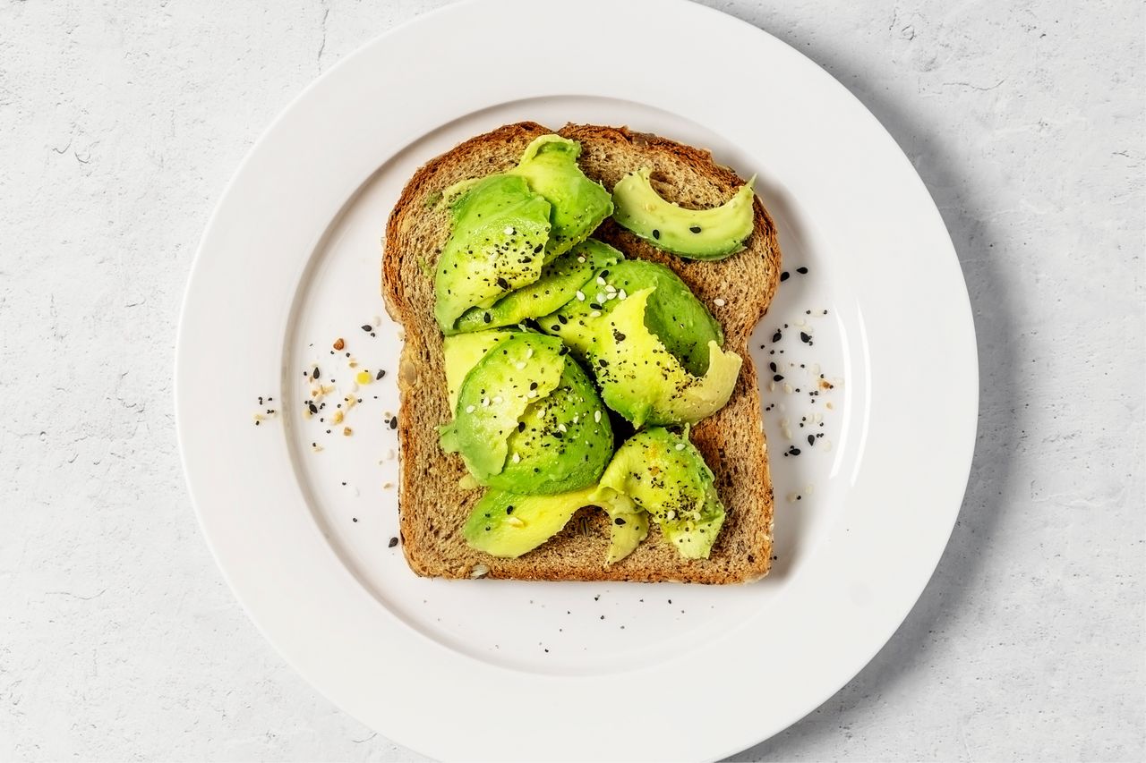 A slice of toast topped with sliced avocado and seasoning served on a white plate