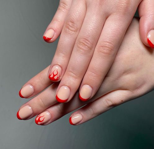 Hands with manicured nails featuring red tips and flame designs on a few nails