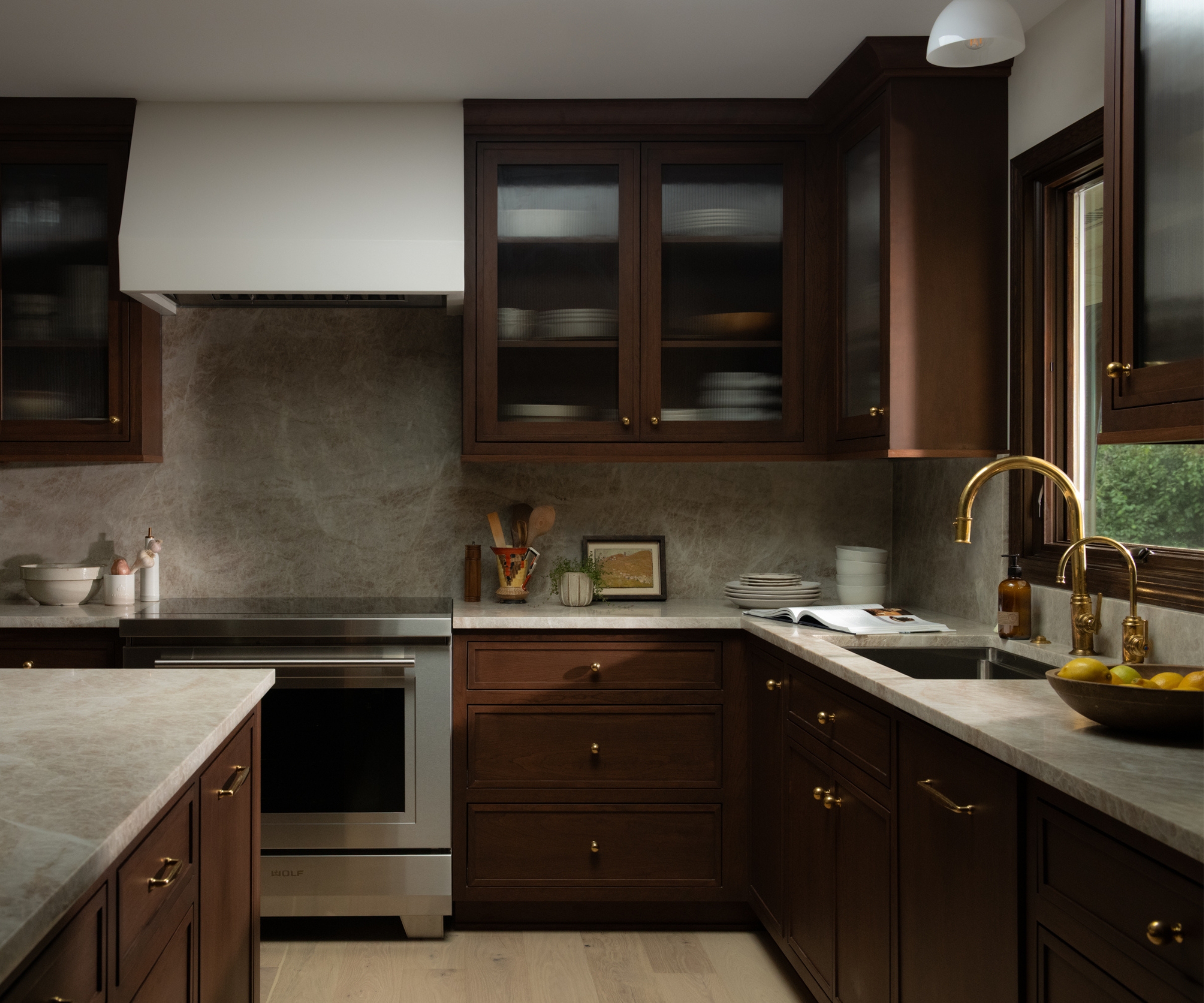 A cherry wood kitchen with a warm white range hood and ceilings, and a marble countersplash
