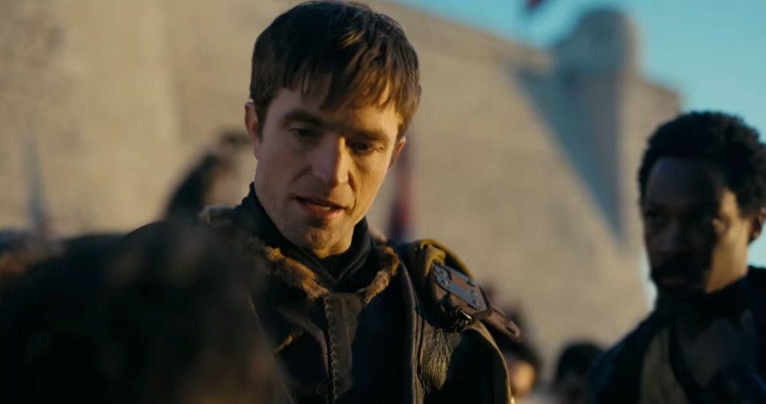 A scene from a historical drama with an actor wearing medieval-style clothing talking to others in a period setting