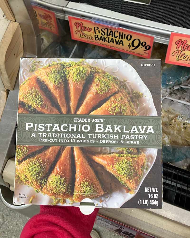Box of Trader Joe's Pistachio Baklava featuring pre-cut wedges topped with pistachios, displayed in a grocery store.