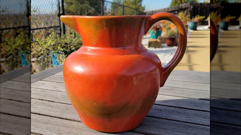 A red-orange Catalina Pottery pitcher on an outdoor table.