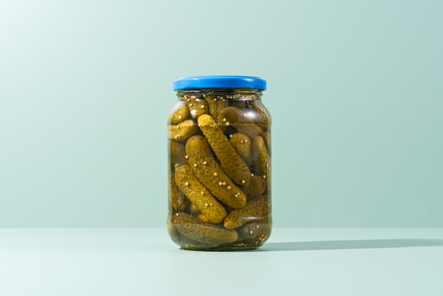 Pickles, Preserved Gherkins in Glass Jar on Green Background