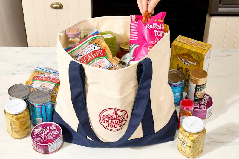 angled shot of an assortment of trader joe's groceries in a khaki and blue trader joe's tote bag - and some of the groceries are scattered around the bag on the counter.