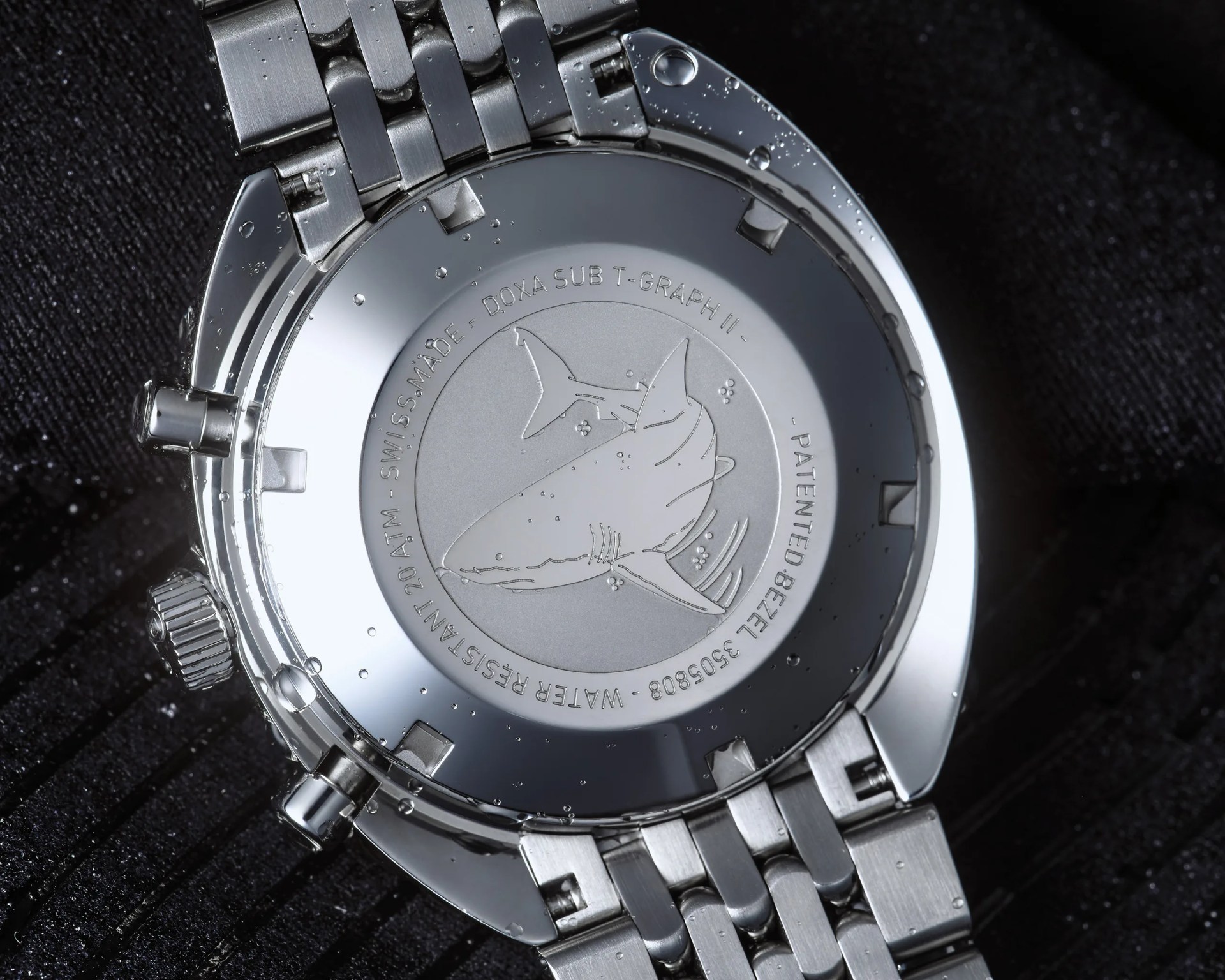 Close-up of the back of a silver Doxa Sub T-Graph II watch with a shark engraving and water droplets on it.