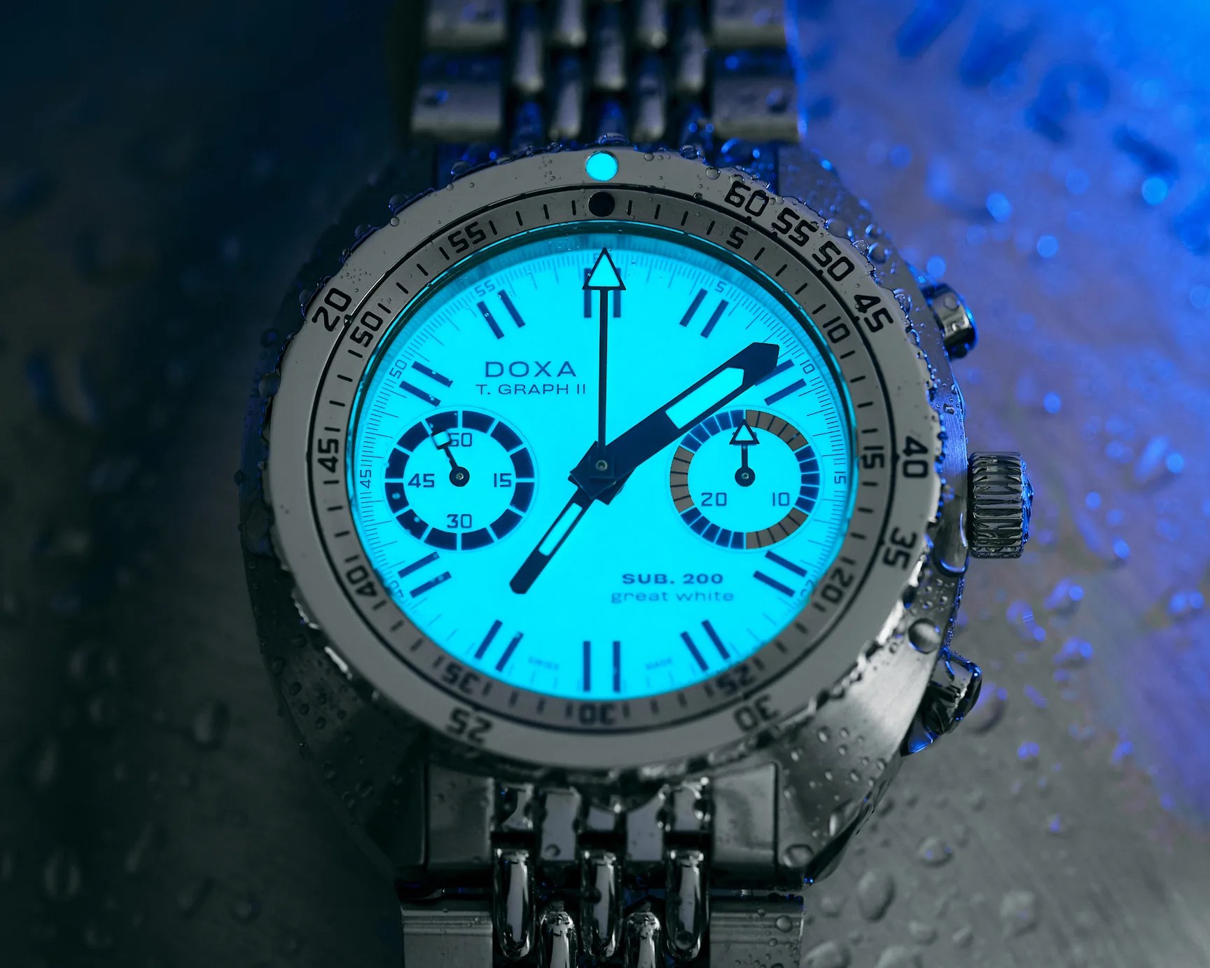 Close-up of a DOXA T. GRAPH II SUB 200 great white watch with luminous blue dial and metal bracelet, covered in water droplets.