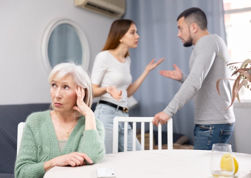 An older woman looks upset as a younger couple argues with hand gestures in the background.
