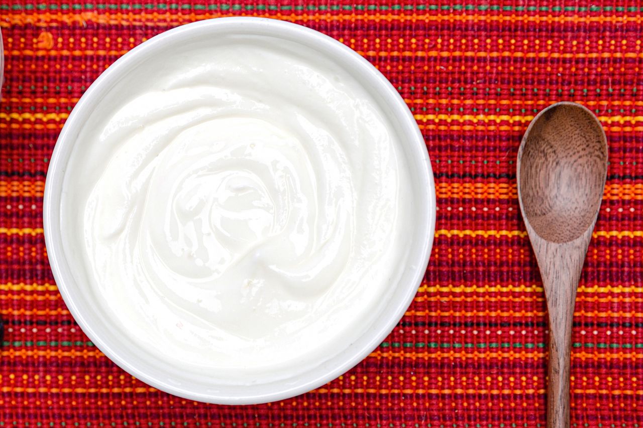A bowl of yogurt next to a wooden spoon on a patterned textile surface