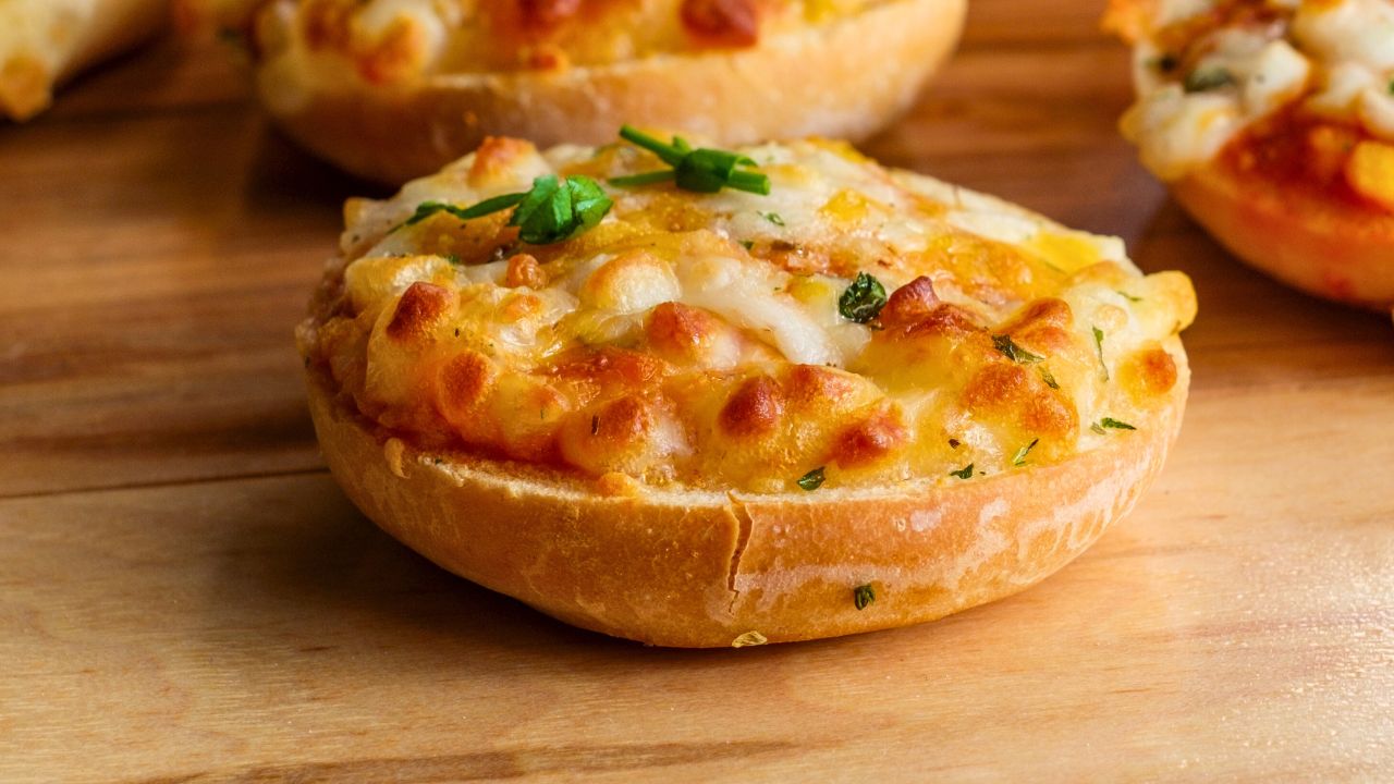 A toasted bread roll topped with melted cheese and herbs on a wooden table.
