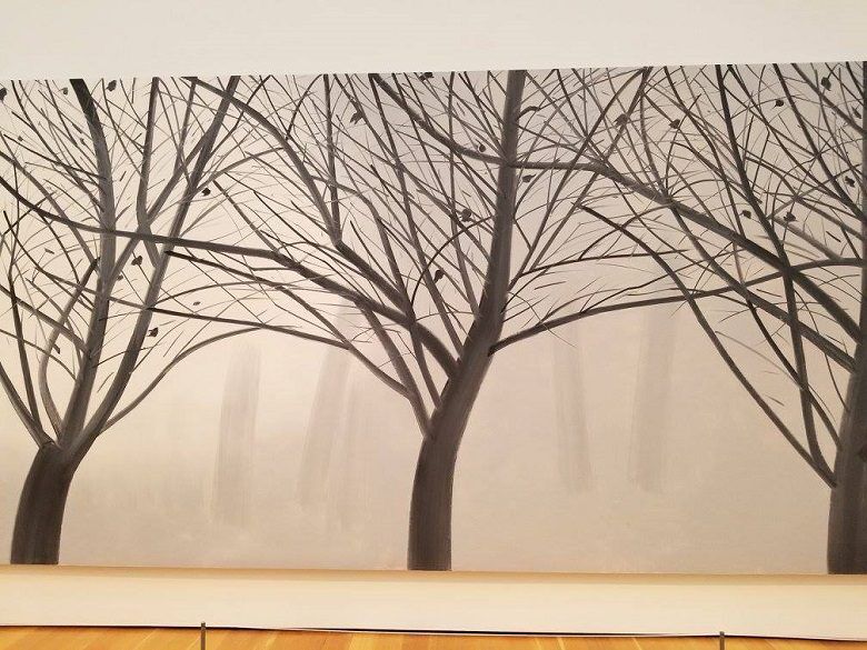 A large monochrome mural at the High Museum of Art in Atlanta, Georgia shows bare tree trunks and a dense web of thin branches fading into a misty background. The sparse leaves and soft gray tones give the gallery installation a quiet winter forest atmosphere.