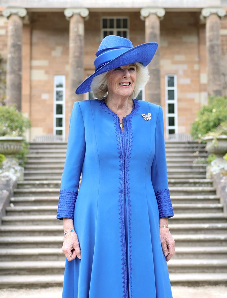 Queen Camilla in a blue jacket and hat smiling