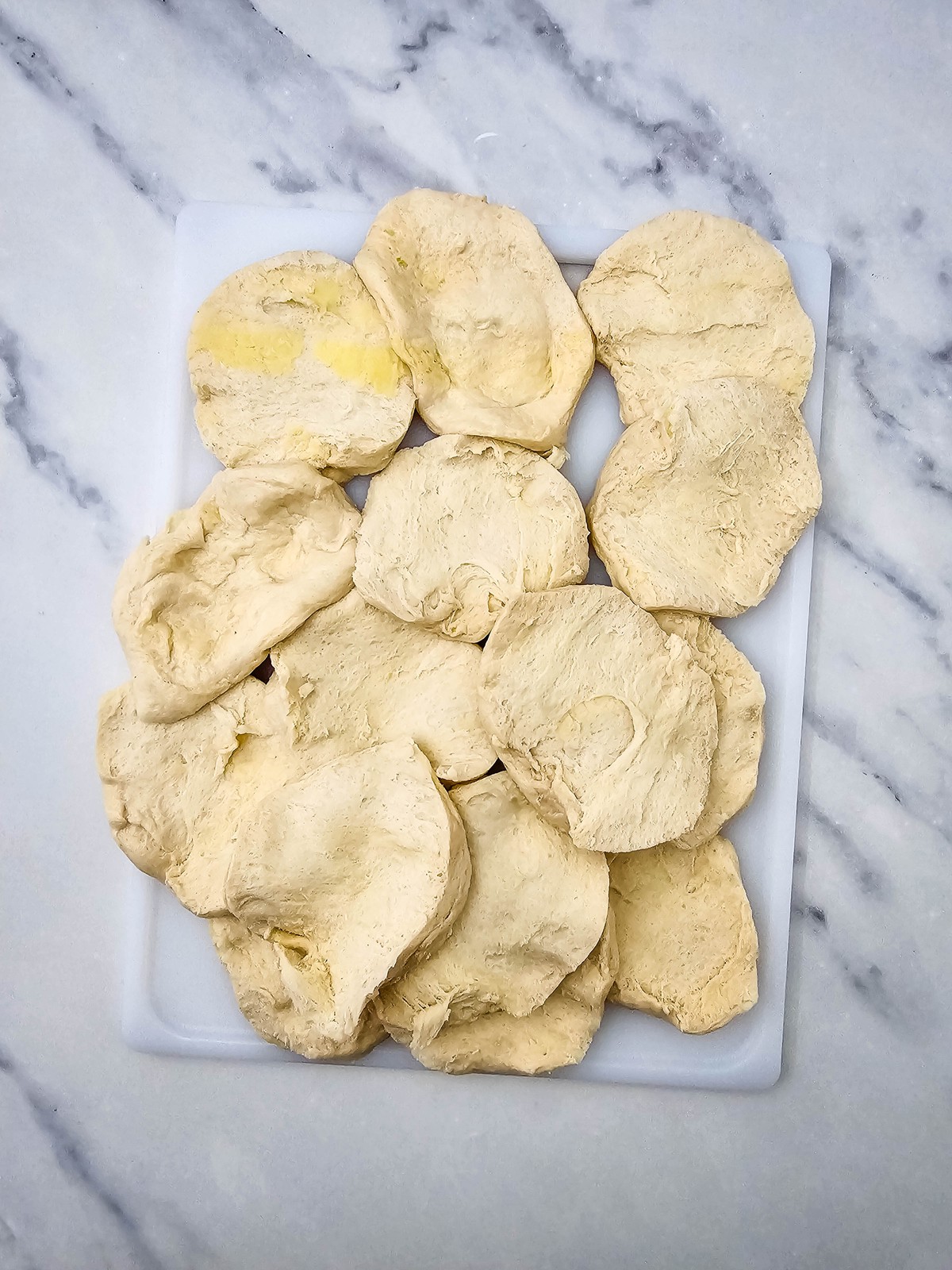 Canned flaky biscuits pulled apart into thin rounds on a cutting board