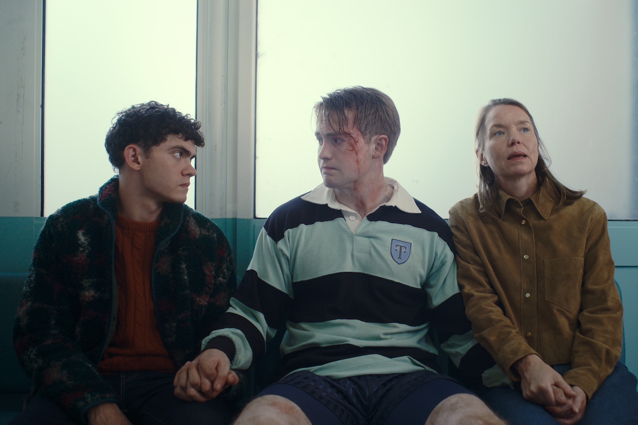 Charlie, Nick, and his mother Sarah sitting together, looking worried, Nick with blood on his face.