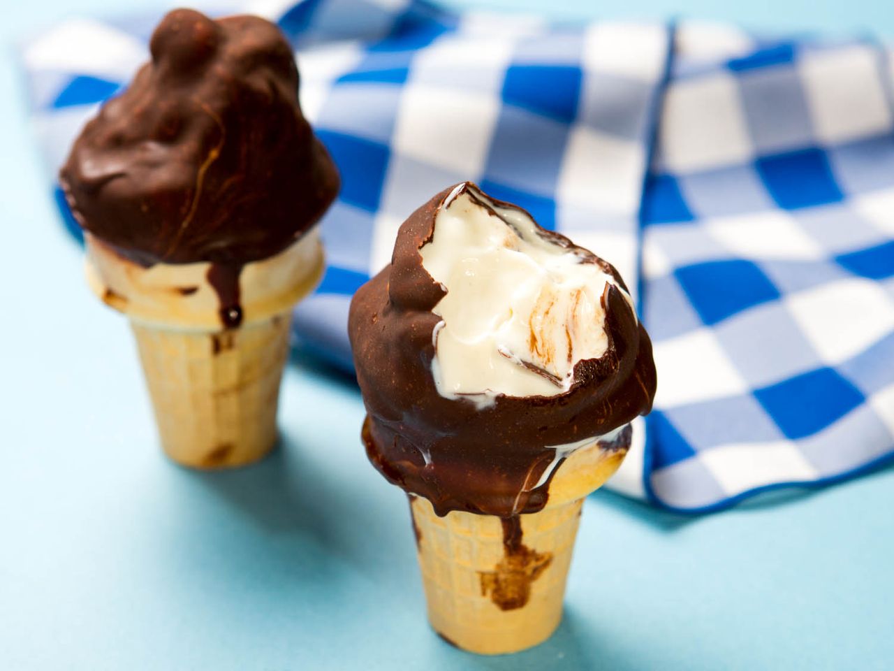 Soft serve ice cream in cones dipped in chocolate with a checkered cloth in the background