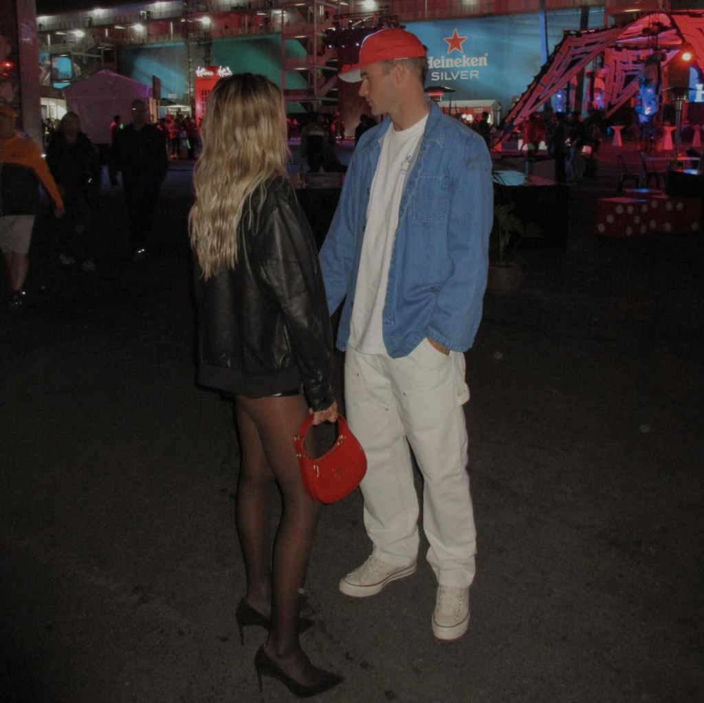 Paige Lorenze and Tommy Paul looking at each other, holding hands, in a dimly lit outdoor setting with a