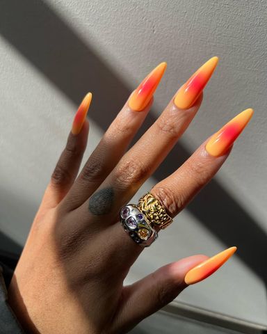 A hand with long styled nails decorated rings on fingers