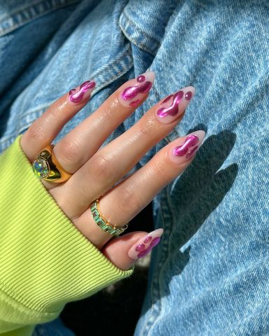 A hand with stylishly designed nails and two rings resting on denim