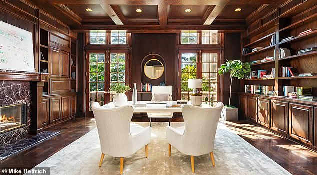 The richly-appointed office features a roaring fireplace enclosed by marble, wood paneling on the ceilings, numerous book shelfs and large French doors that lead to a terrace outside