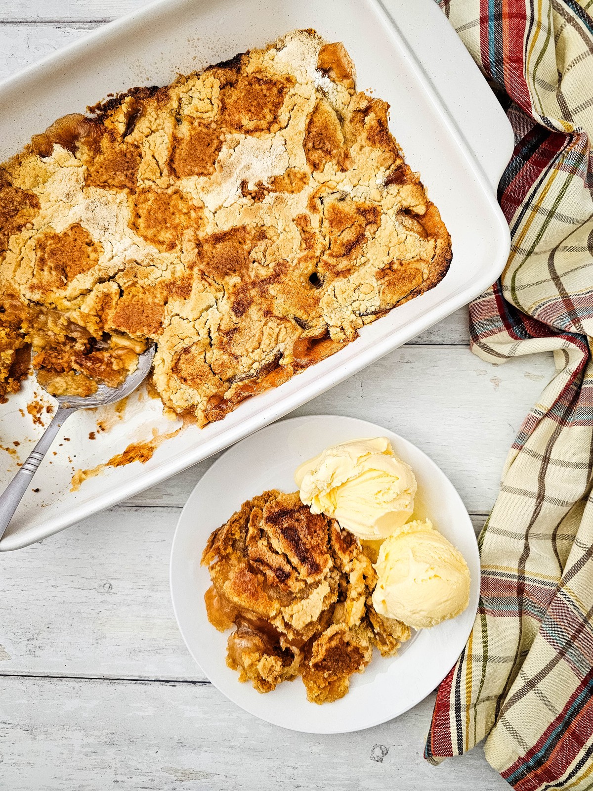 Baked apple dump cake in a white dish with a plated serving and vanilla ice cream