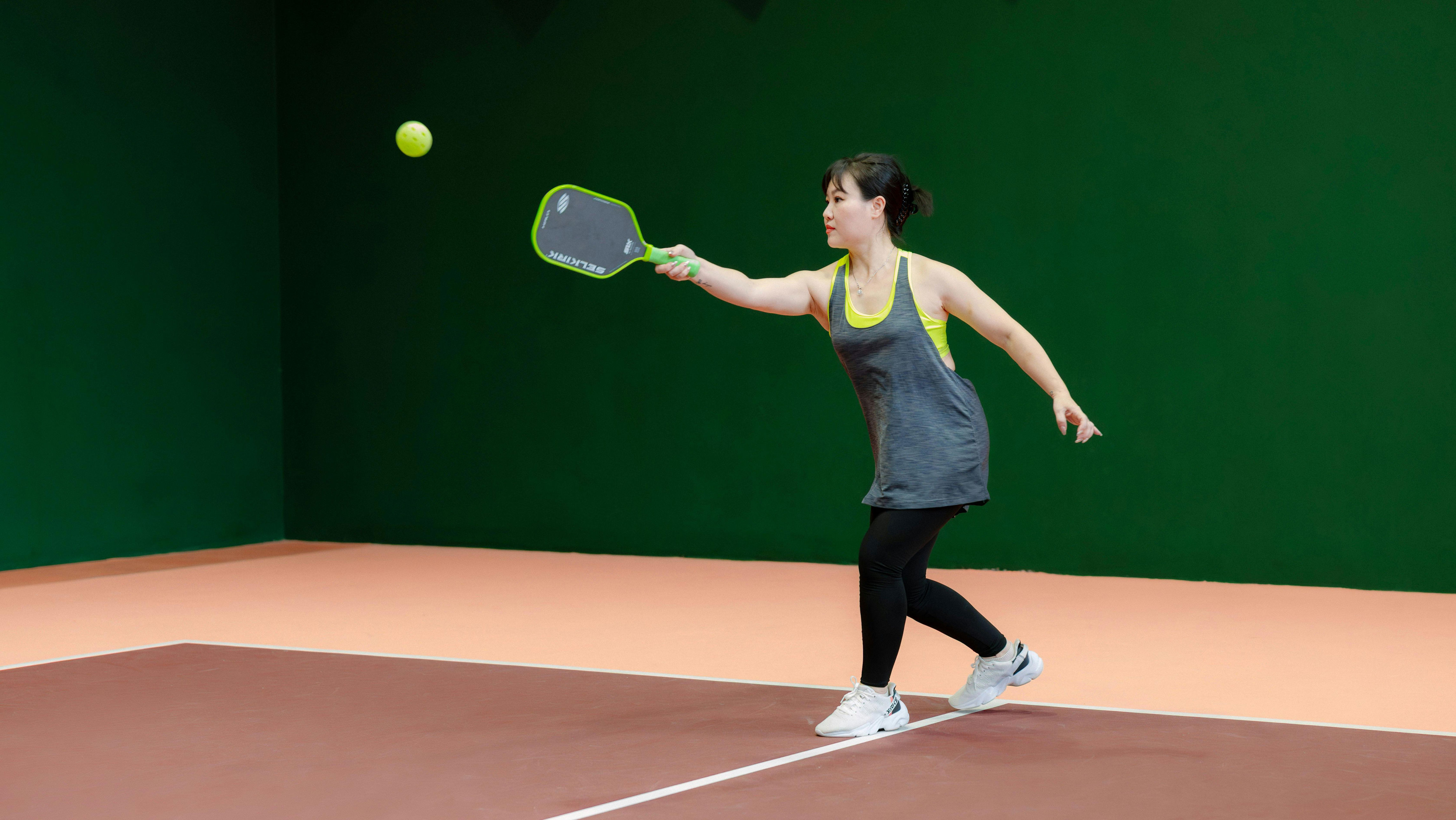 Girl playing pickleball, holding a paddle and hitting a ball on the court.