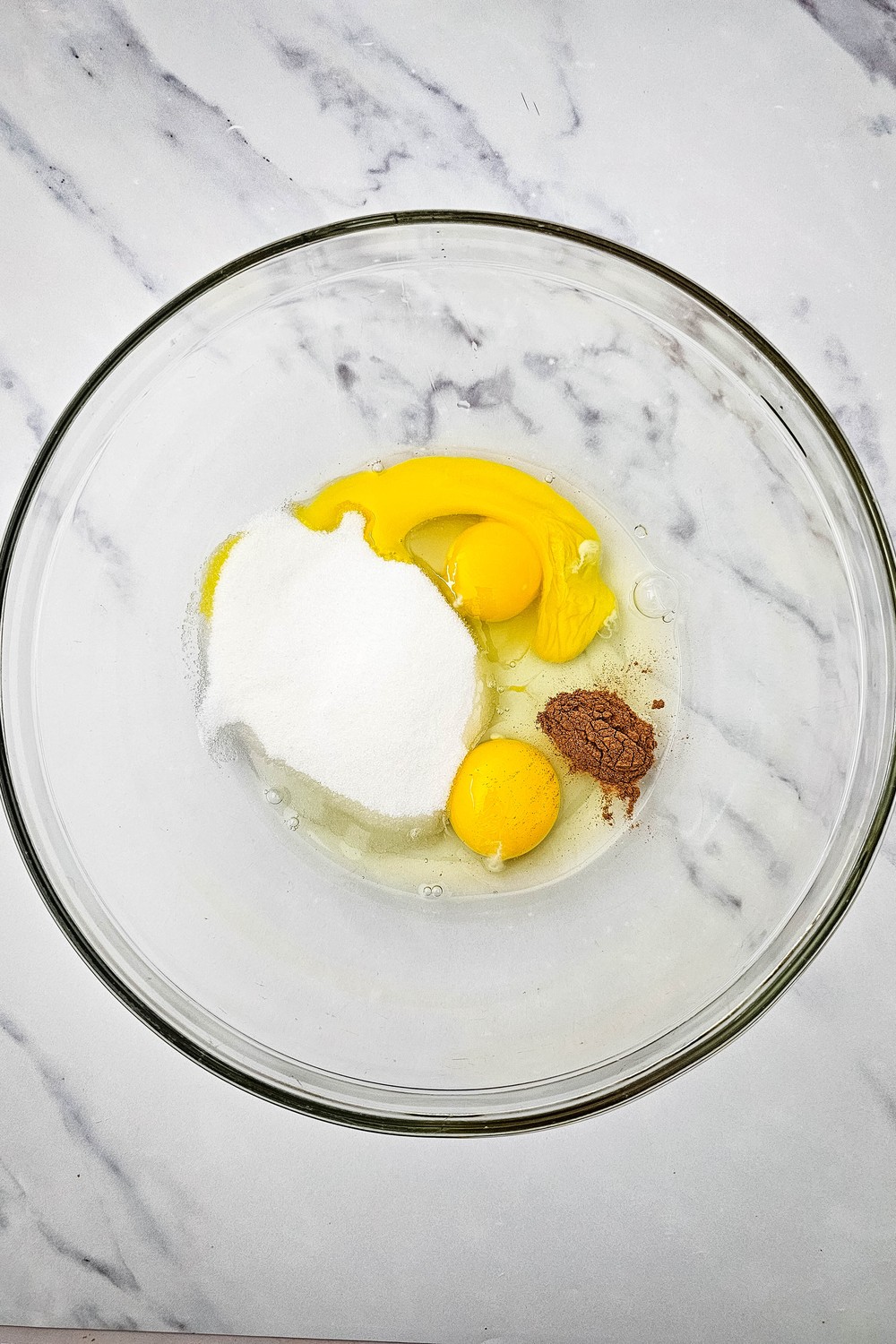 Eggs, sugar and cinnamon in a glass mixing bowl