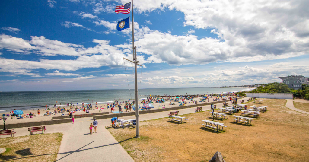 An American flag and a NH state flag fly on a flagpole above Wallis Sands Beach in Rye, New Hampshire.