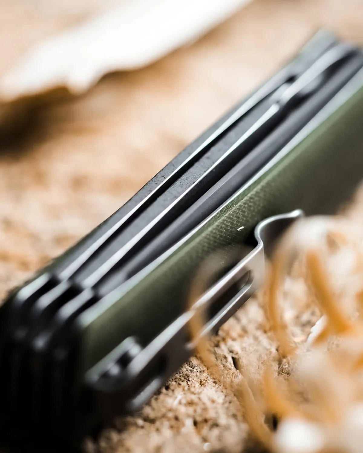 Close-up of a green and black folding knife handle with a metal clip on a textured surface.