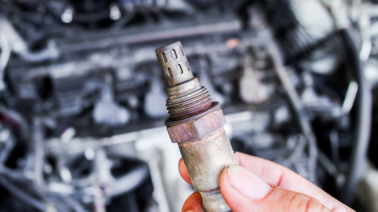 Hand holds used oxygen (O2) sensor of car engine above engine