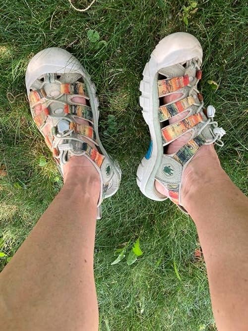 Person wearing casual open-toe sandals with woven straps standing on grass