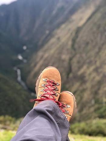 Hiking boots with red laces rest over a scenic mountain view, suggesting leisure and adventure