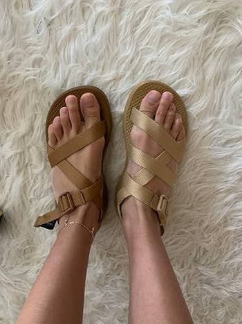 Feet wearing strappy sandals with adjustable buckles on a fluffy carpet, showcasing relaxed and casual footwear style