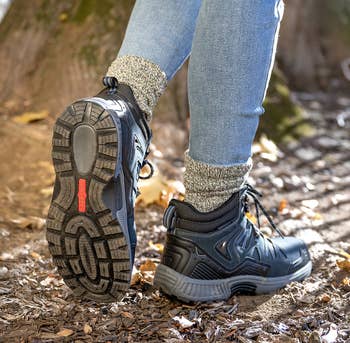 Close-up of a person wearing black hiking shoes and jeans, walking on a trail surrounded by fallen leaves