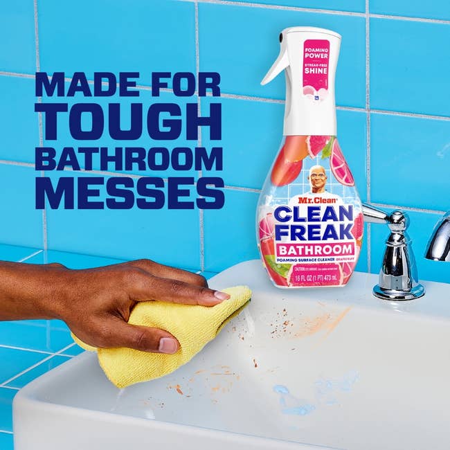Hand cleaning a sink with a yellow cloth, using Mr. Clean Clean Freak Bathroom spray. Text: