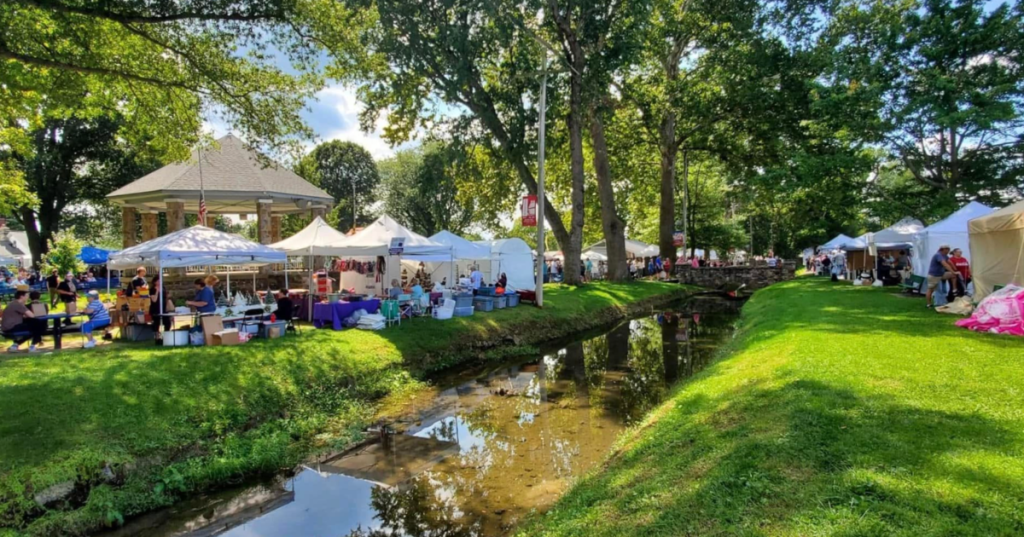 Crowds browse vendor tents at a festival in Shafer Park, Boonsboro, Maryland, beside a small creek.