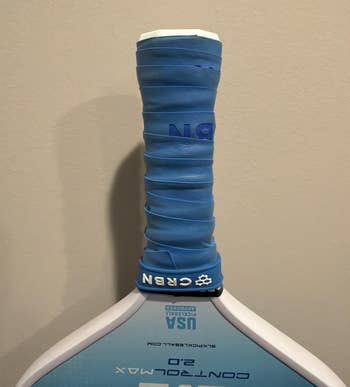 Close-up of a pickleball paddle handle with a blue grip, showing branding and