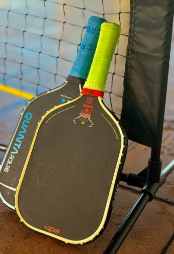 Two pickleball paddles leaning against a net on a court