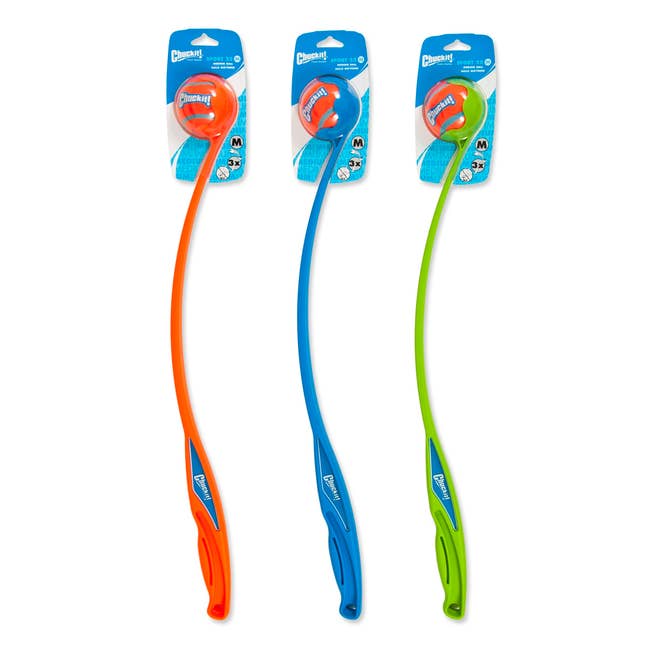 Three Chuckit! ball launchers in orange, blue, and green, each with a ball. Designed for effortless fetch, the launchers have ergonomic handles