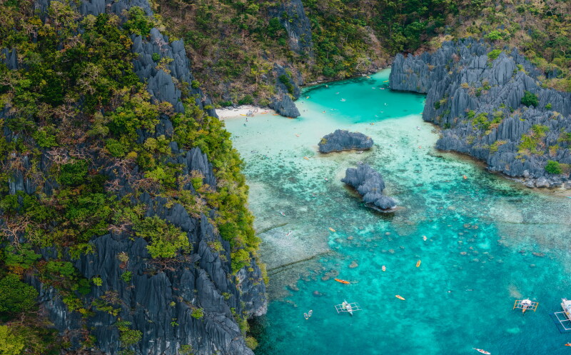 Overhead view of a coastal cove in Palawan, Philippines, with turquoise water, some scattered boats, and soaring gray cliffs